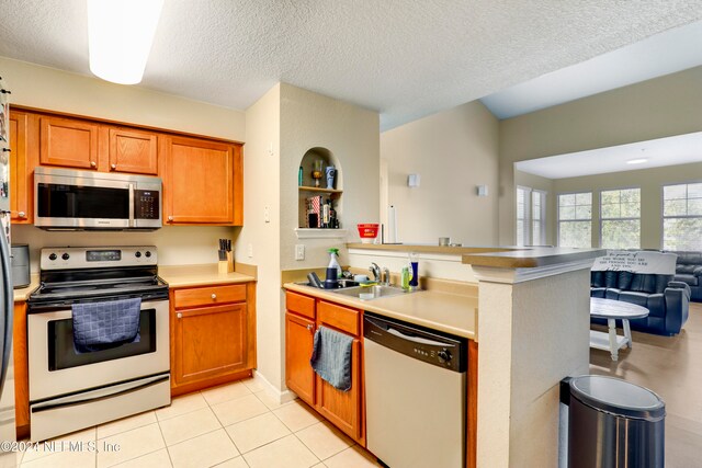 kitchen featuring sink, stainless steel appliances, kitchen peninsula, a textured ceiling, and light tile patterned floors