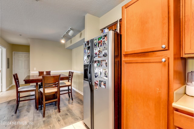 kitchen featuring stainless steel refrigerator with ice dispenser, a textured ceiling, light hardwood / wood-style floors, and track lighting