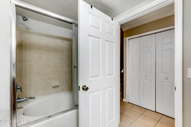 bathroom with tile patterned flooring, shower / bath combination with glass door, and a textured ceiling