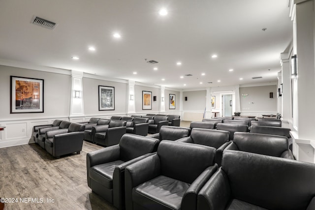 cinema room featuring ornate columns, ornamental molding, and light hardwood / wood-style flooring