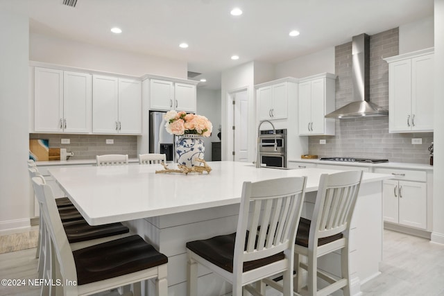 kitchen with wall chimney exhaust hood, a kitchen bar, white cabinetry, and a large island with sink