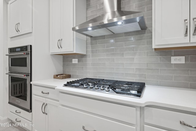 kitchen with backsplash, white cabinets, wall chimney exhaust hood, and appliances with stainless steel finishes