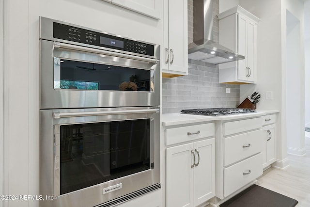 kitchen with white cabinetry, wall chimney range hood, light hardwood / wood-style flooring, decorative backsplash, and appliances with stainless steel finishes