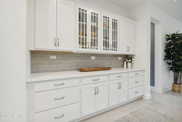 bar featuring decorative backsplash, white cabinets, and light wood-type flooring