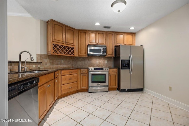 kitchen with sink, decorative backsplash, dark stone countertops, light tile patterned floors, and appliances with stainless steel finishes