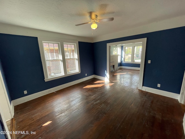 empty room featuring a textured ceiling, a fireplace, ceiling fan, and dark wood-type flooring