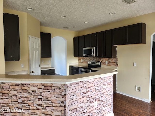 kitchen with kitchen peninsula, dark hardwood / wood-style flooring, stainless steel appliances, and a textured ceiling