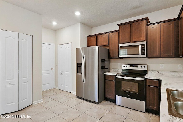 kitchen featuring dark brown cabinets, light tile patterned floors, and stainless steel appliances