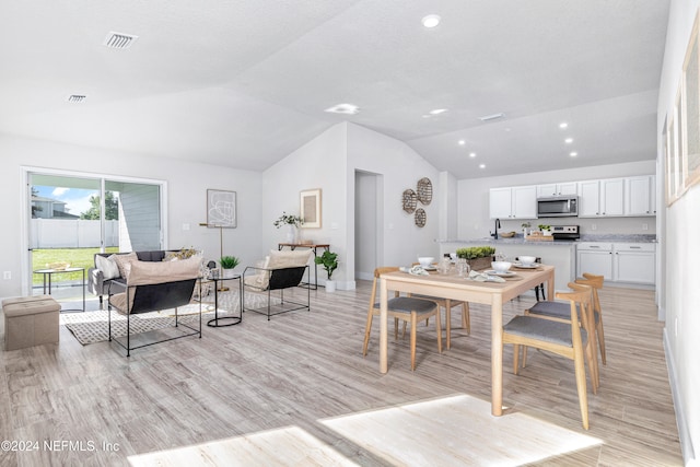 dining area featuring light wood-type flooring, sink, and vaulted ceiling