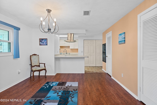 interior space with dark wood-type flooring, sink, black appliances, white cabinets, and hanging light fixtures