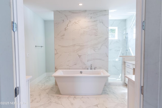 full bath featuring a freestanding tub, marble finish floor, vanity, stone wall, and recessed lighting