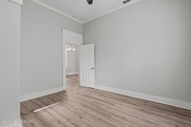 empty room with light hardwood / wood-style flooring, ornamental molding, and a notable chandelier