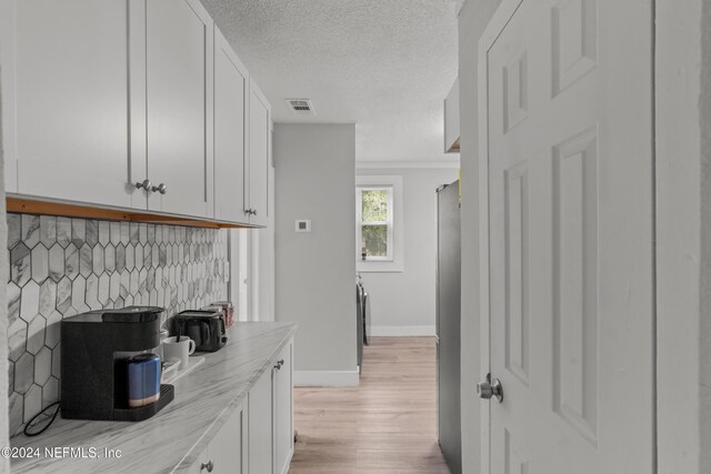 kitchen featuring white cabinetry, light stone counters, backsplash, a textured ceiling, and light wood-type flooring