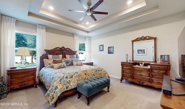 carpeted bedroom with a tray ceiling, multiple windows, and ceiling fan