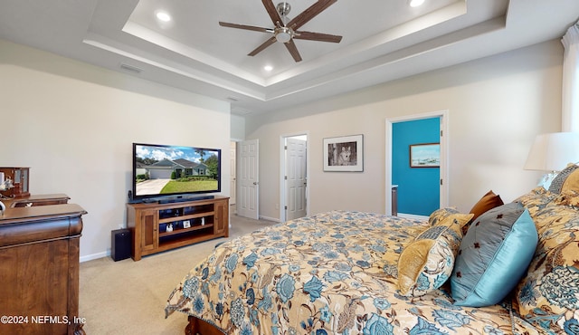 carpeted bedroom featuring a tray ceiling, ensuite bathroom, and ceiling fan