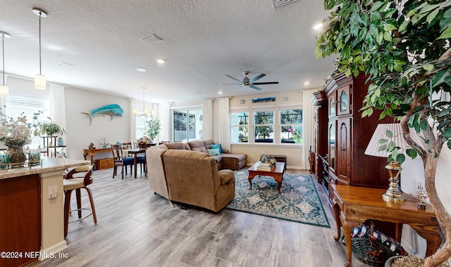 living room with a textured ceiling, light hardwood / wood-style flooring, and ceiling fan with notable chandelier