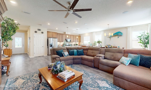 living room featuring plenty of natural light, ceiling fan with notable chandelier, and a textured ceiling