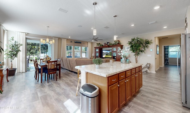 kitchen featuring a center island with sink, light stone countertops, hanging light fixtures, and a wealth of natural light