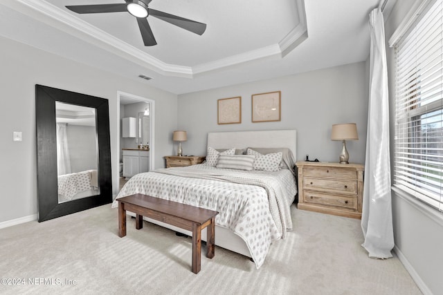 bedroom with light carpet, a tray ceiling, ceiling fan, crown molding, and connected bathroom