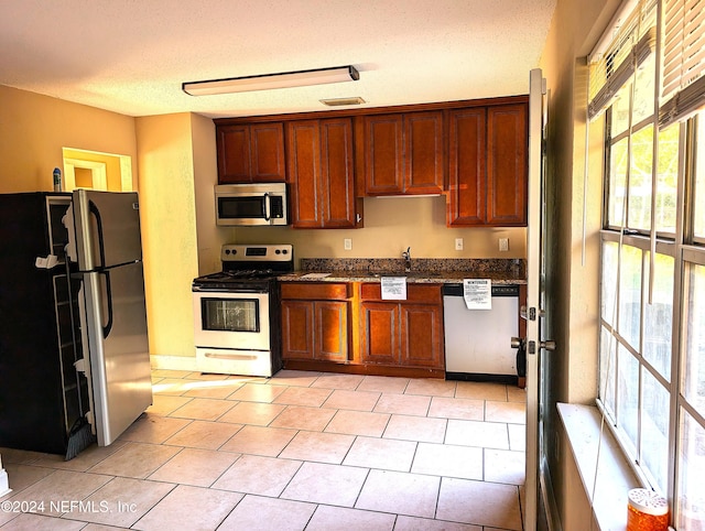 kitchen with a textured ceiling, sink, light tile patterned floors, and stainless steel appliances