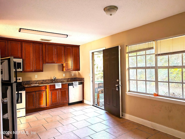 kitchen featuring sink, a textured ceiling, appliances with stainless steel finishes, and dark stone counters