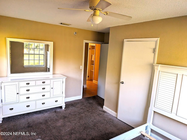 unfurnished bedroom with ceiling fan, dark carpet, and a textured ceiling