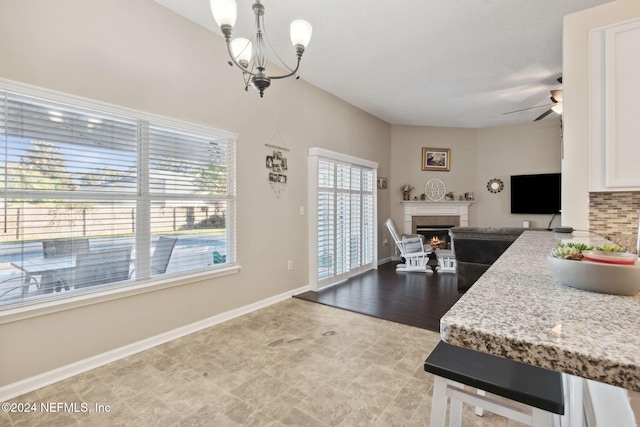 kitchen featuring light stone counters, decorative light fixtures, a fireplace, ceiling fan with notable chandelier, and light wood-type flooring