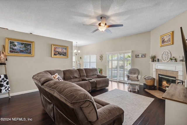 living room featuring ceiling fan with notable chandelier, dark hardwood / wood-style flooring, a textured ceiling, and a tiled fireplace