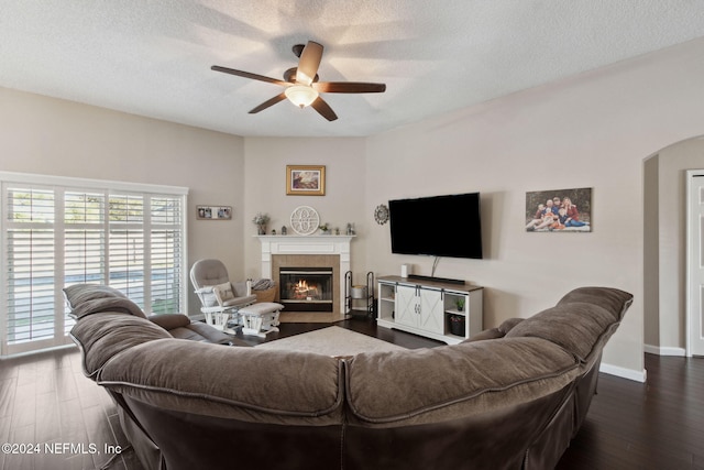 living room featuring a tile fireplace, a textured ceiling, dark hardwood / wood-style flooring, and ceiling fan