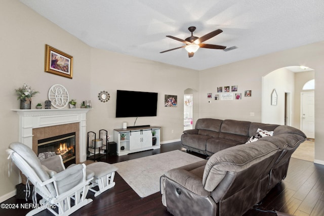 living room with a tile fireplace, a textured ceiling, dark hardwood / wood-style flooring, and ceiling fan