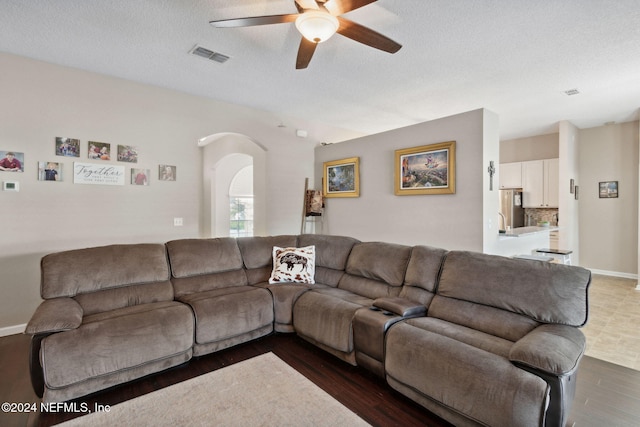 living room with a textured ceiling, dark hardwood / wood-style flooring, and ceiling fan