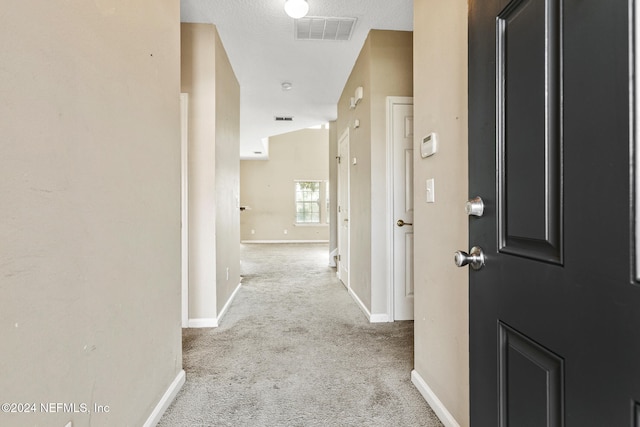 hallway with a textured ceiling, lofted ceiling, and light carpet