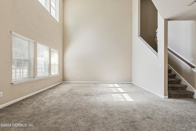 unfurnished living room with carpet flooring, a towering ceiling, and a textured ceiling