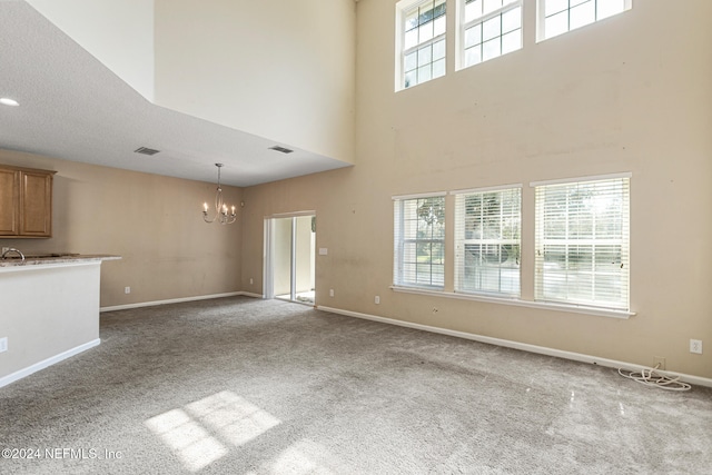 unfurnished living room featuring carpet, a high ceiling, a textured ceiling, and an inviting chandelier