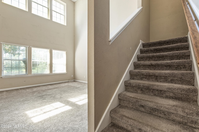 stairway with carpet flooring, a healthy amount of sunlight, and a high ceiling