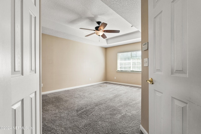 spare room with carpet flooring, a textured ceiling, a tray ceiling, and ceiling fan