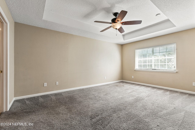 empty room with a raised ceiling, ceiling fan, carpet floors, and a textured ceiling