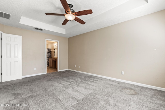 unfurnished bedroom with a textured ceiling, connected bathroom, a raised ceiling, and ceiling fan