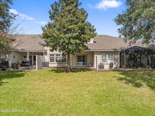 rear view of property featuring a lawn, glass enclosure, and central AC