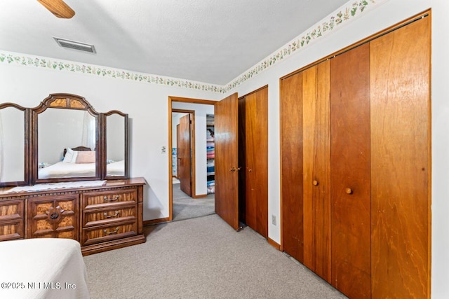 bedroom with light colored carpet, ceiling fan, a textured ceiling, and multiple closets