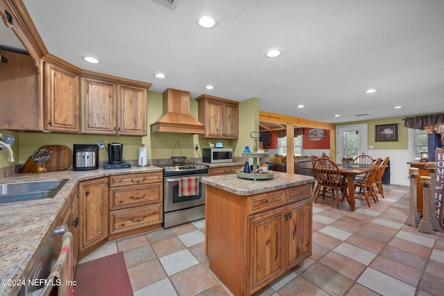 kitchen with sink, a center island, stainless steel appliances, light stone counters, and custom exhaust hood