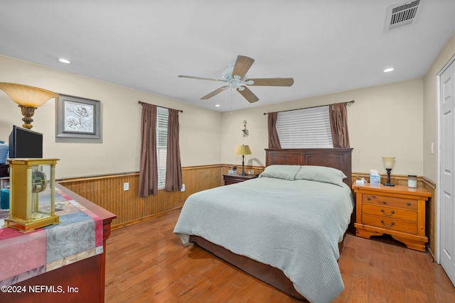 bedroom featuring light hardwood / wood-style flooring, ceiling fan, and wooden walls