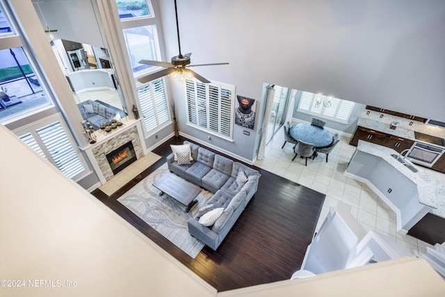 living room with tile patterned floors, ceiling fan with notable chandelier, a stone fireplace, and a high ceiling