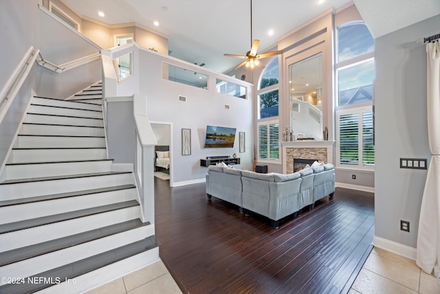 living room with hardwood / wood-style floors, ceiling fan, a stone fireplace, and a towering ceiling