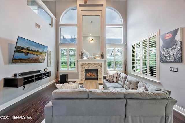 living room featuring dark hardwood / wood-style floors, ceiling fan, a stone fireplace, and a high ceiling