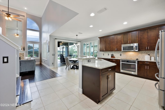 kitchen with appliances with stainless steel finishes, light stone counters, ceiling fan, a center island with sink, and light tile patterned flooring