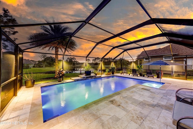 pool at dusk featuring a lawn, glass enclosure, and a patio area