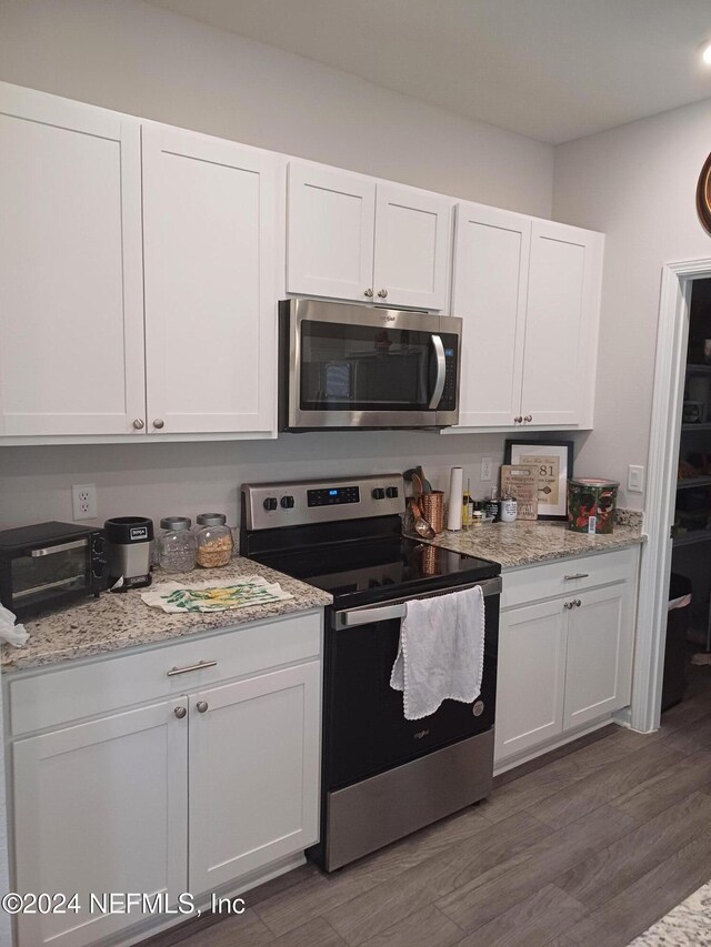 kitchen featuring light stone countertops, white cabinetry, stainless steel appliances, and dark wood-type flooring