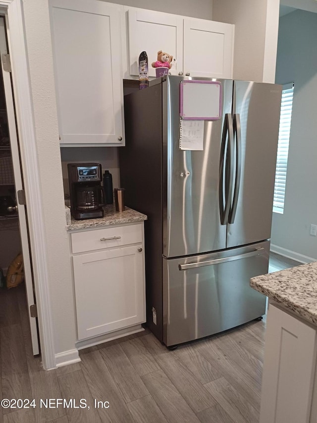 kitchen with white cabinets, stainless steel fridge, light hardwood / wood-style floors, and light stone counters