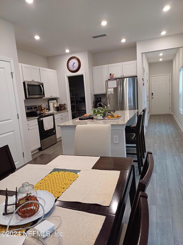 kitchen featuring a center island with sink, white cabinets, dark hardwood / wood-style floors, light stone countertops, and appliances with stainless steel finishes